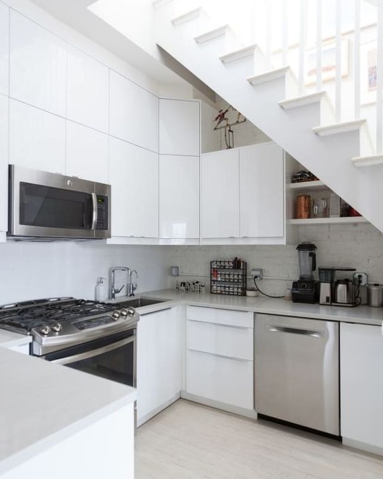 a simple white Scandinavian kitchen placed partly under the stairs to save some space, with a brick backsplash