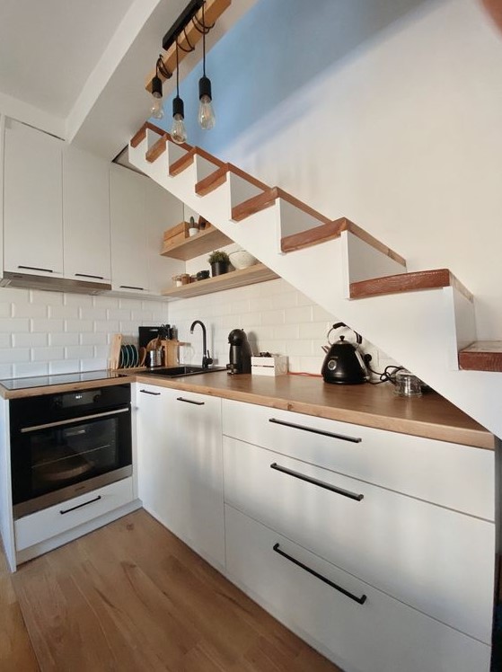 a small Scandi kitchen under the stairs, with butcherblock countertops and a white brick backsplash, pendant bulbs