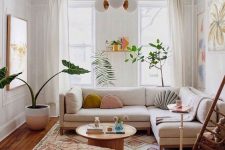 a small boho living room with a white sectional, a printed boho rug and a pouf, some bright art, pillows and a chandelier