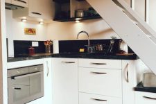 a small kitchen built under the staircase, with white cabinets and black countertops, built-in lights is a lovely space