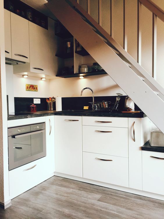 A small kitchen built under the staircase, with white cabinets and black countertops, built in lights is a lovely space