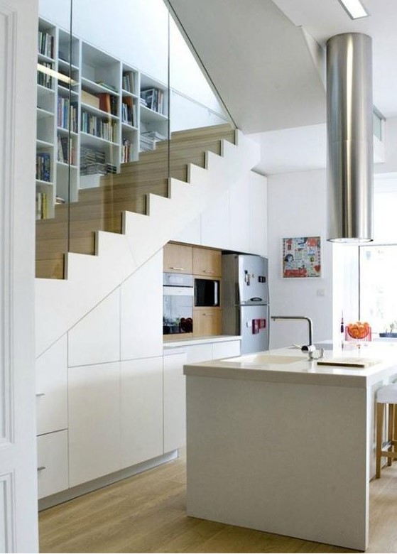a small modern kitchen in white built in under the staircase, with a large kitchen island, a hood over it and some appliances