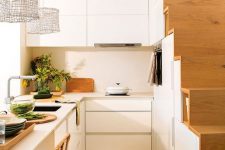 a small modern white kitchen partly built into the staircase, with a kitchen island that doubles as a dining zone