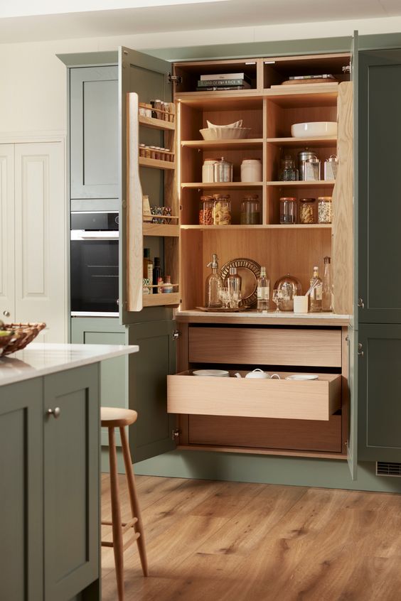 a small yet functional built-in pantry with stained shelves and a shelving unit on the door, drawers and some tableware and spices