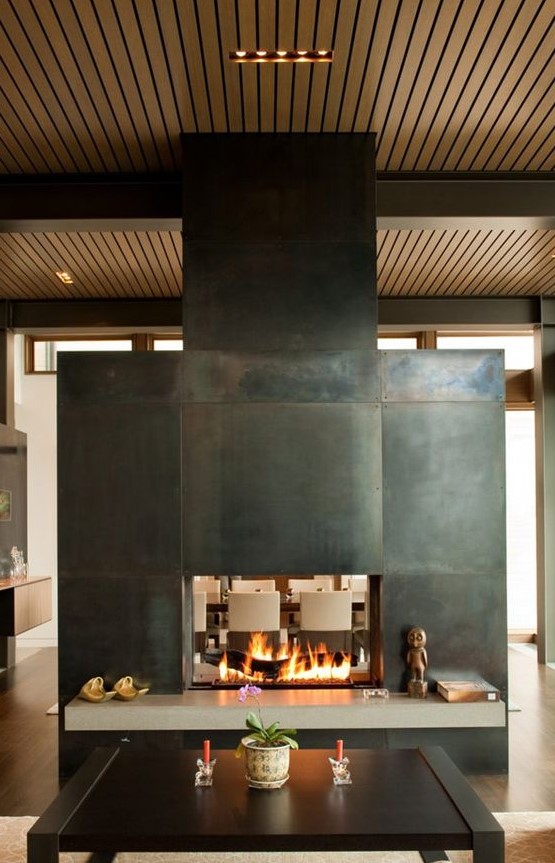 A stunning two sided fireplace clad with metal sheets to separate the living and dining room and give coziness to both
