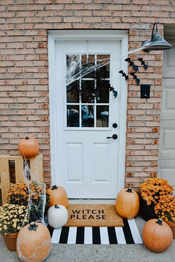 a stylish Halloween front porch with orange pumpkins, bats, web and bright potted flowers