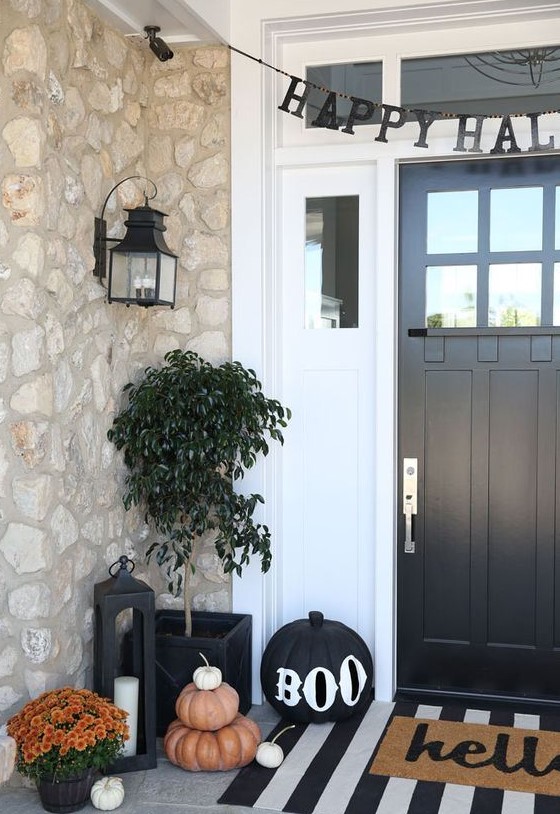 a stylish Halloween porch with stacked pumpkins and a black one, a paper bunting and some bright flowers