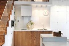a stylish Nordic kitchen with stained lower cabinets, a staircase that hisde a lot of storage space, a white kitchen island with a table