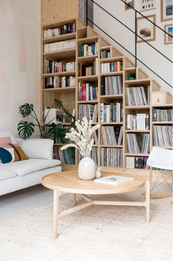 a stylish mid-century modern space with a bookcase staricase, a sofa, a round table and a comfy chair is very chic and practical