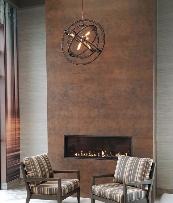 A stylish modern living room with a built in fireplace clad with copper and a metal sphere chandelier looks very cool
