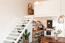 a stylish modern loft with a kithen squeezed under the stairs, open storage units and potted greenery, a dining space next to it