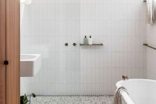 a stylish neutral bathroom with white skinny tiles, a white terrazzo floor, a vintage tub and a white wall-mounted sink