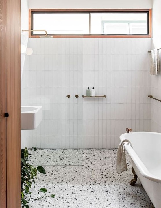 A stylish neutral bathroom with white skinny tiles, a white terrazzo floor, a vintage tub and a white wall mounted sink