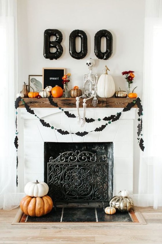 a stylish rustic Halloween mantel with black balloons, a bat bunting, lots of pumpkins, a skeleton and blooms