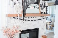 a traditional Halloween mantel with black bat garlands, black spiders, a skeleton, some witches’ hats and a mirror with decor