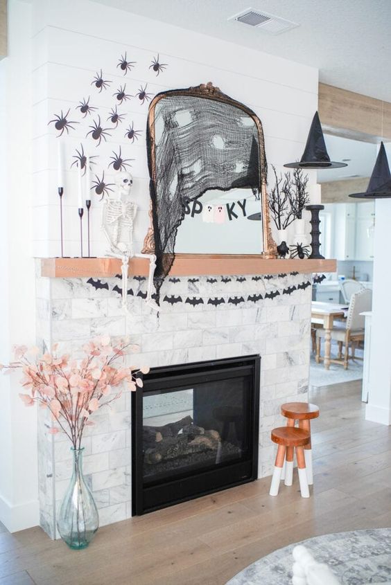 a traditional Halloween mantel with black bat garlands, black spiders, a skeleton, some witches' hats and a mirror with decor