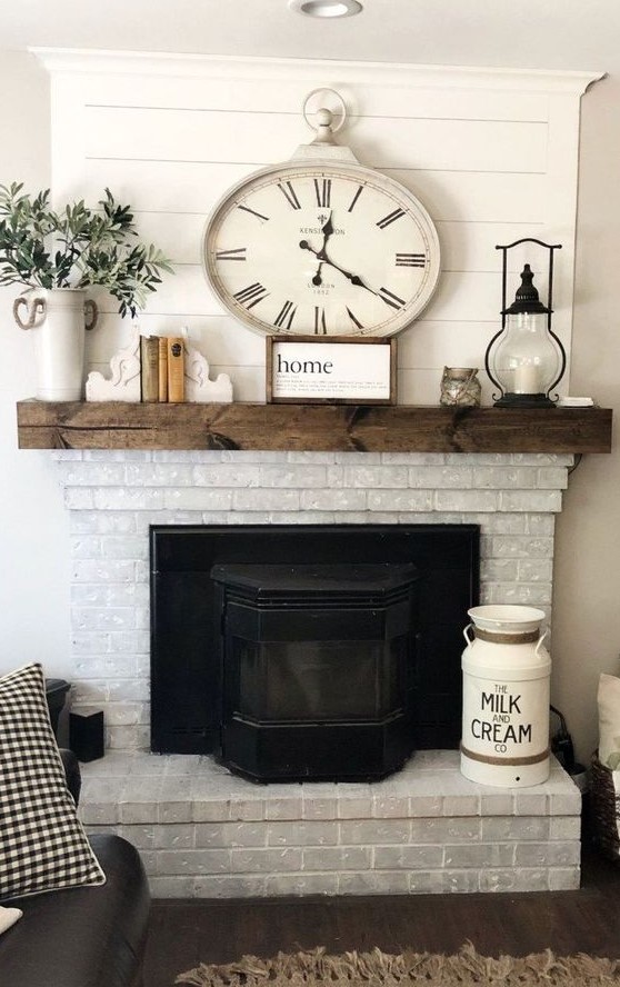 A vintage farmhouse fireplace of whitewashed brick, a dark stained wooden mantel with pretty vintage decor