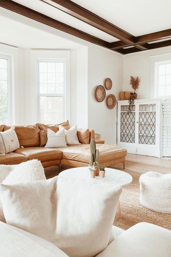 a welcoming boho living room with dark beams, a leather sofa, white furniture and decorative baskets on the wall