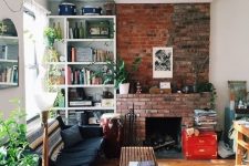 a welcoming mid-century modern living room with a red brick fireplace, a black sofa, a stained bench and built-in shelves plus greenery