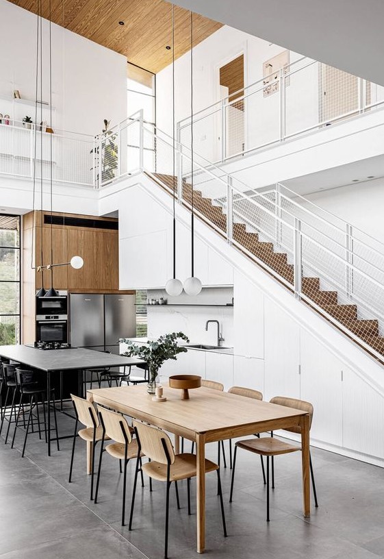 A white Scandinavian kitchen built into the staircase, with built in appliances, a kitchen island and a dining zone