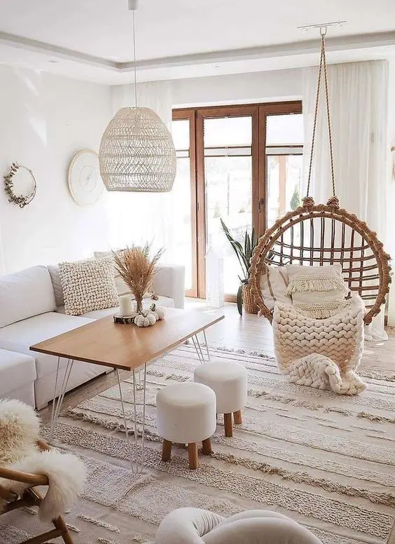 a white boho living room with a white sofa, a table with hairpin legs, a woven pendant chair, a macrame rug