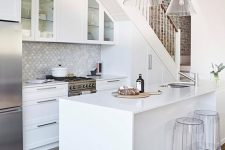 a white modern farmhouse kitchen placed under the stairs with cabinets built in, a scallop tile backsplash, a kitchen island