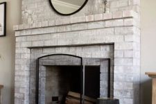 a whitewashed brick fireplace with a brick mantel, a round mirror, a metal frame and a candle lantern is stylish
