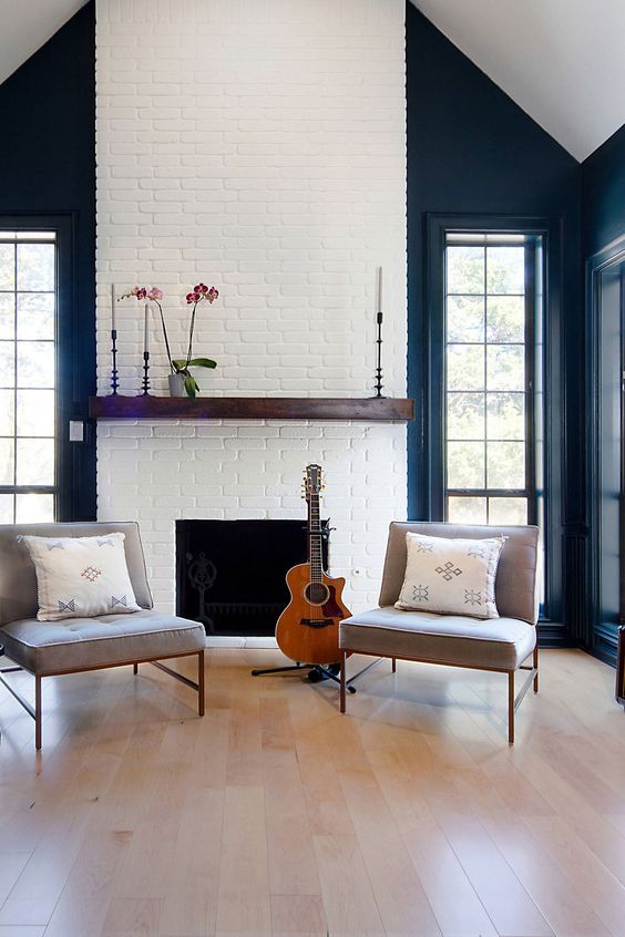 an attic living room with black walls, a white brick fireplace with a mantel and minimal styling, grey chairs