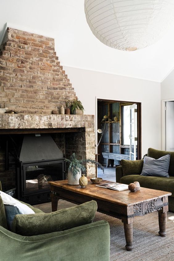 an eclectic living room with a brick fireplace, a stained table, green sofas and a jute rug and a paper pendant lamp