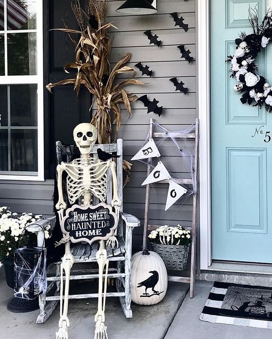 an elegant black and white Halloween porch with a skull wreath, a skeleton, a web candle lantern and some white blooms