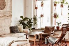 an elegant boho living room with rattan and wood furniture, boho rugs and pillows, planters in macrame hangers and a macrame hanging on the wall
