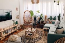 an eye-catching boho living room with a green sectional, a pallet TV unit, a boho printed rug, pillows, a lot of plants and a catchy pendant lamp