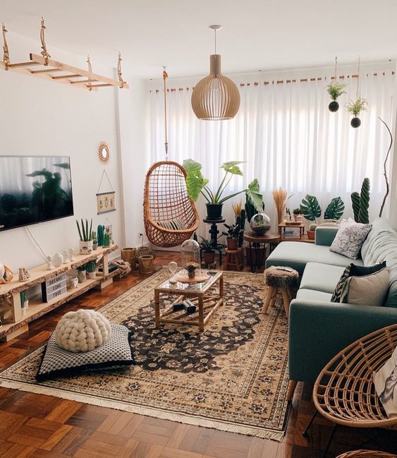 an eye-catching boho living room with a green sectional, a pallet TV unit, a boho printed rug, pillows, a lot of plants and a catchy pendant lamp