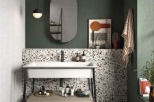 an eye-catchy bathroom with a dark green accent wall, catchy terrazzo tiles on the floor and wall and a cool free-standing sink