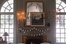 simple and classic Halloween decor with tall and thin candles in black candleholders, a ghost garland and a spooky artwork