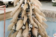 a Christmas tree decorated with pampas grass, metallic ornaments and calligraphy ones is a lovely boho decor idea