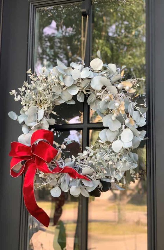a catchy modern Christmas wreath of pale greenery, berries and a bold red bow is a bright and lovely idea