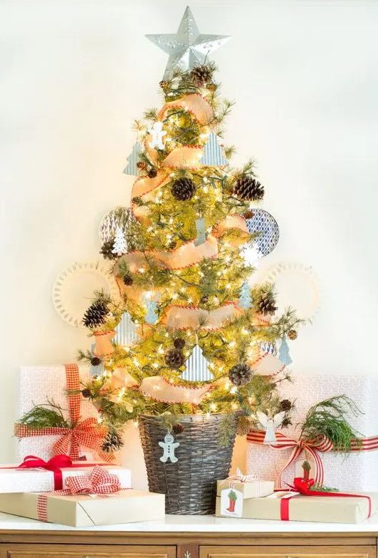 A chic and beautiful Christmas tree in a basket, with pinecones, mini tree shaped ornaments, snowflakes and lights plus a star topper