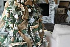 a chic and shiny Christmas tree with burlap ribbons, pompom garlands, snowflakes, white and silver ornaments and pinecones