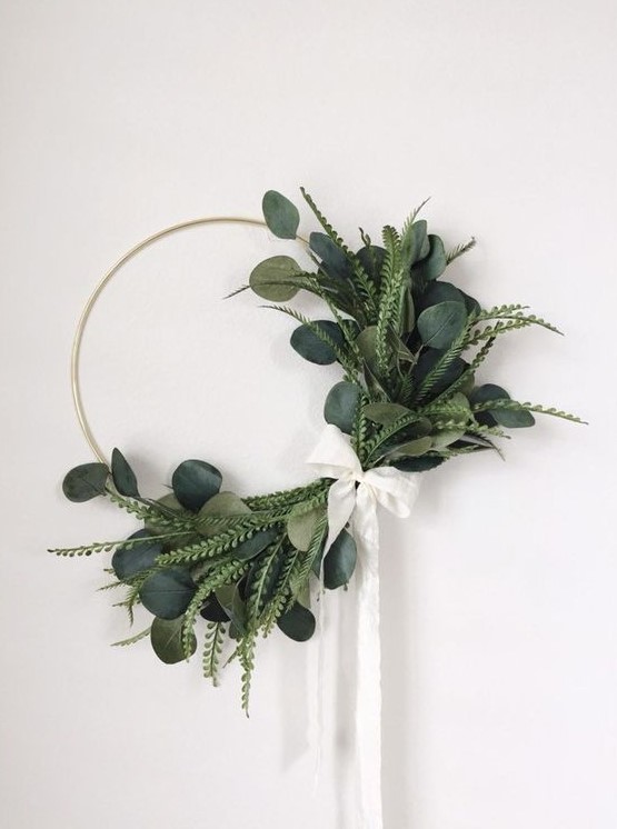 a cool modern Christmas wreath with several types of greenery attached only on one side, with a white ribbon bow
