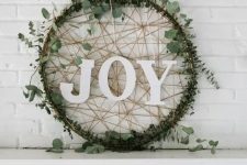 a creative modern Christmas wreath of an embroidery hoop, covered with eucalyptus, yarn and with letters looks awesome