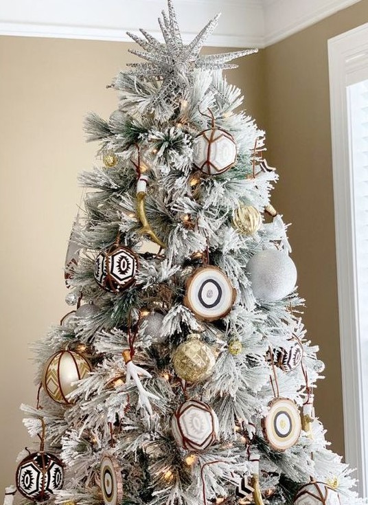 A flocked Christmas tree with white glitter ornaments, gold ones, agate slices and gold antlers plus lights is very free spirited