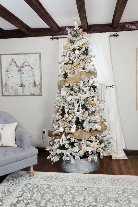 a flocked farmhouse Christmas tree with burlap ribbon, white and silver ornaments, lights and striped ribbons