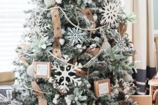 a flocked farmhouse Christmas tree with pale greenery, large cardboard snowflakes, burlap ribbons and little signs in frames