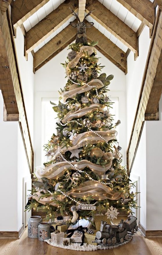 a gorgeous rustic Christmas tree with burlap ribbons, beaded garlands, lights, snowflakes, stockings and pale leaves plus a deer head