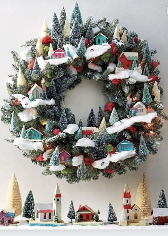 A jaw dropping modern Christmas wreath of evergreens, little colorful houses and bottle brush trees is wow