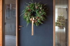 a lush modern Christmas wreath with lush greenery, some white blooms, pinecones and a peachy pink ribbon bow