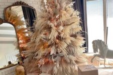 a luxurious pampas grass Christmas tree decorated with lights, neutral and pink blooms and fronds and topped with a gold star