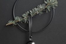a minimalist Christmas wreath in black with an evergreen branch and a black bell hanging on a black leather loop