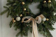 a modern Christmas wreath of evergreens and eucalyptus, white and gold ornaments and a ribbon bow is super cool